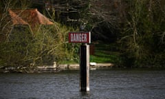 A sign reading 'danger' in the River Thames with a bird sitting on top of it.