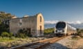 Train passing a derelict station at Lumio in the Balagne region of Corsica with snow covered mountains in the distance under a depp blue sky<br>HP6CFK Train passing a derelict station at Lumio in the Balagne region of Corsica with snow covered mountains in the distance under a depp blue sky