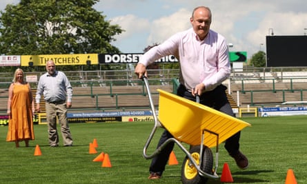 Ed Davey takes part in a wheelbarrow race at Huish Park, home of Yeovil Town football club, 17 June 2024.