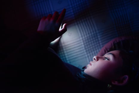 A child stares at a smartphone in a darkened room.