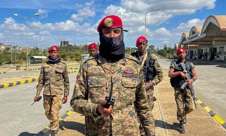 An Ethiopian soldier in fatigues and a red beret holds a radio as four fellow soldiers behind him look on.