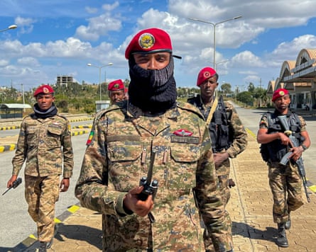 An Ethiopian soldier in fatigues and a red beret holds a radio as four fellow soldiers behind him look on.