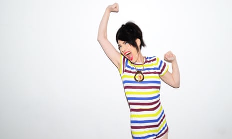 Kathleen Hanna with her mouth open as if shouting, punching the air and showing hair under her raised arm