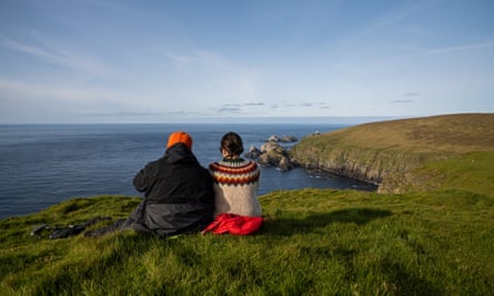A couple sit on a top of cliff and admire the landscape w Hermaness National Nature Reserve, Unst Island, Shetlands.