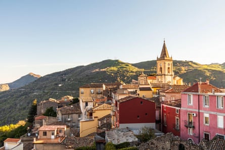 A pretty hilltop town with pink and yellow fronted buildings and a stone church tower