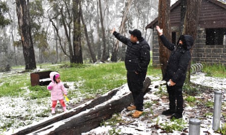 a man and a woman watch their toddler daughter playing in the scattered snow