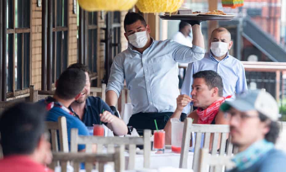 A waiter wearing masks and gloves delivers food to customers seated at an outdoor patio in Washington DC, on 29 May. 