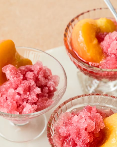 Three glass dessert bowls filled with pink granita and peach slices on a white plate