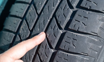A person points with his index finger to a car tire worn out by time and use