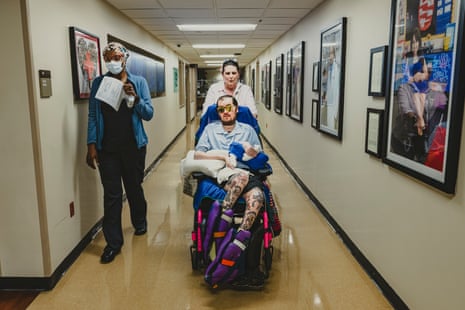 A mother wheeling her son in doctor’s office, a nurse walking alongside them