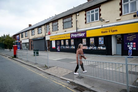 A low-rise terrace of shops with one closed behind shutters. A large Premier supermarket stretches down the street.