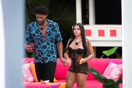 A man in a Hawaiian shirt and a woman hold hands standing in front of a neon couch