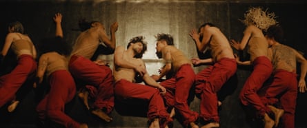 Eight men sleeping, topless, wearing red pyjama bottoms, lying on their sides photographed from above