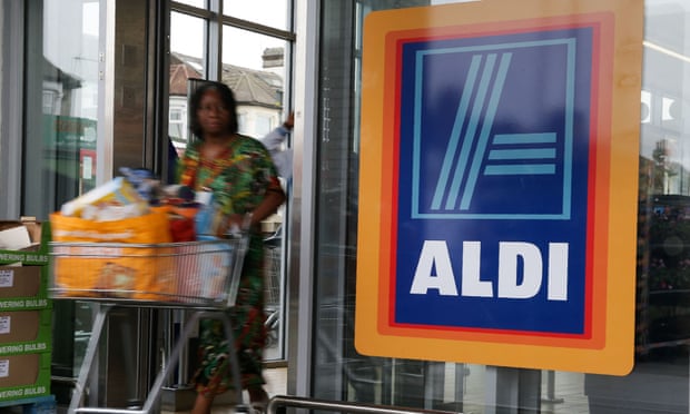 A woman pushes a shopping trolley past an Aldi logo as she leaves a supermarket in London