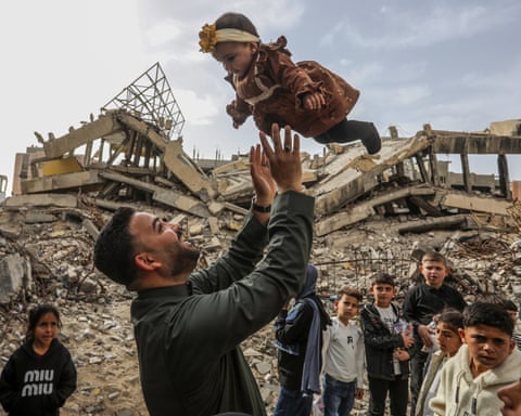A man tosses a child in the air amid rubble in Gaza, with several children watching