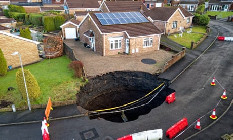 Sinkhole surrounded by plastic fences and cones in the driveway of a bungalow