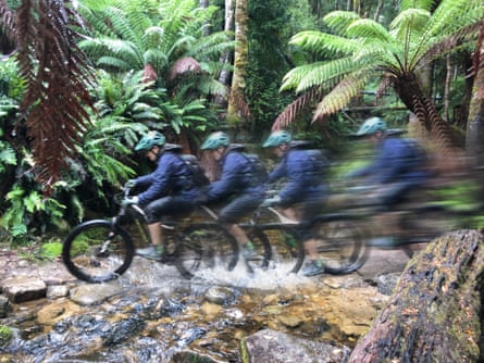 Slow-shutter speed photo capturing a mountain biker riding at speed over a rocky creek.