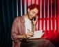 Smiling male entrepreneur talking on smart phone and writing in diary while sitting on seat