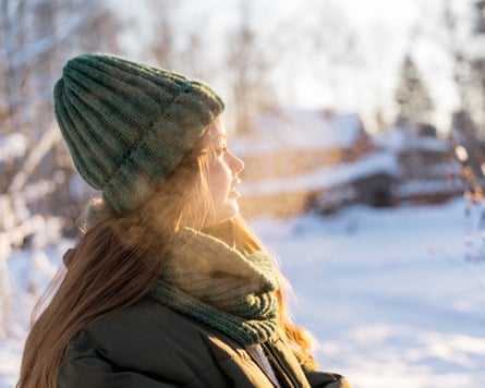 Portrait of a teenage girl in casual winter fashion walking among tall trees in sunny cold snow forest.