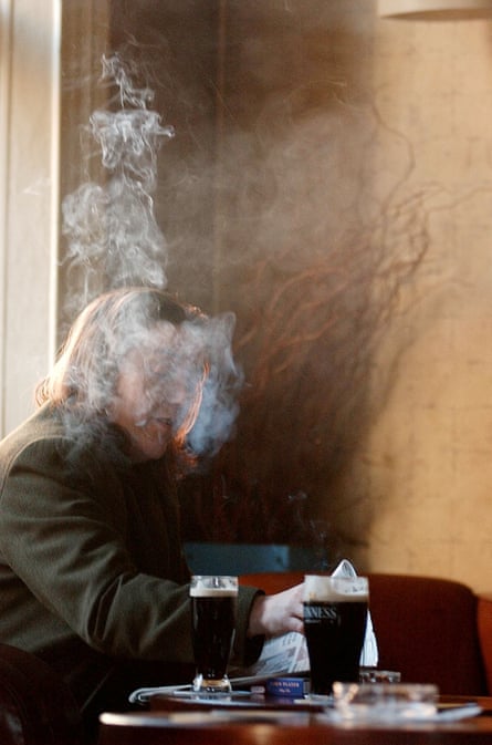 A person sits in a pub, shrouded in cigarette smoke with beer on the table in front of them