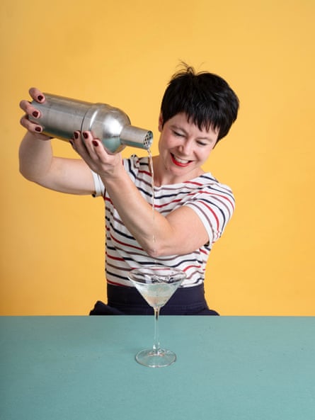 Rachel Dixon smiling and holding a cocktail shaker up high aas she pours a drink into a martini glass