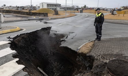 A wide and deep crack in the road, with smaller cracks and damage to the road in the distance