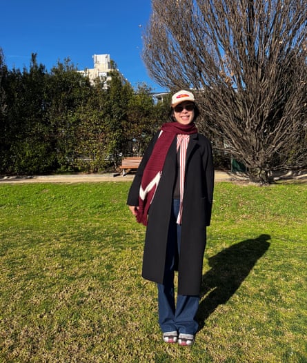Maggie Zhou wears a trucker cap, black coat, long scarf and jeans.