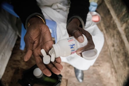 A woman pours large white tablets into the palm of one hand from a small white plastic bottle.