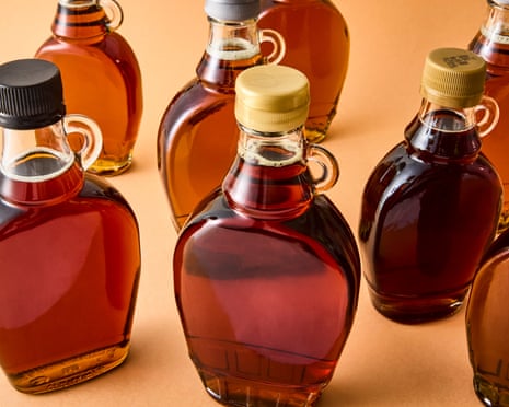 Seven glass jugs filled with amber maple syrup in varying shades stand on an orange surface