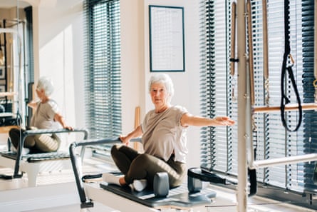 An older woman sitting cross-legged on a reformer machine.
