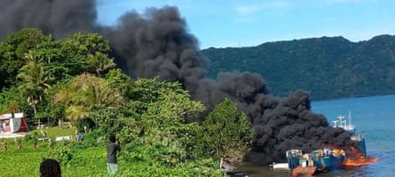 Locals look on as thick black smoke billows from the ship