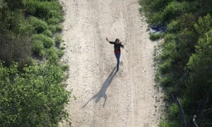 An undocumented migrant raises her hands as a US Customs and Border Protection helicopter flies overhead, near McAllen, Texas in March.