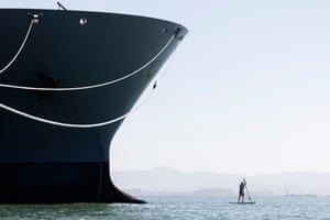 The front of a ship towers over a lone paddleboarder
