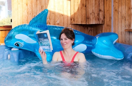 Emine reads a novel resting her head on a blow-up shark in a hot tub