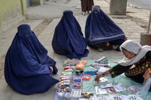 Three women in blue burqas sit by a collection of beauty accessories on a blanket