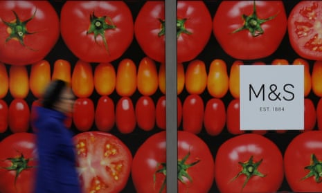 A woman passes an M&S shop window poster of rich red ripe tomatoes