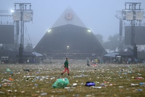 A festivalgoer walks past litter-strewn ground at the Glastonbury festival with the Pyramid Stage in the background