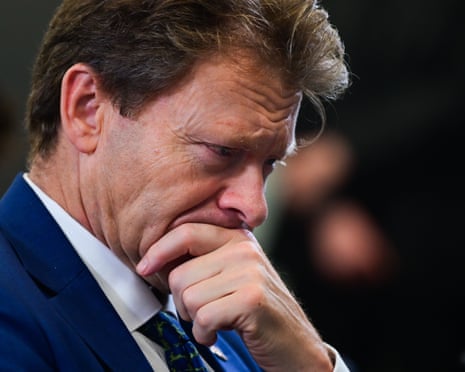 Tice rests his chin on his hand, looking down with a furrowed brow