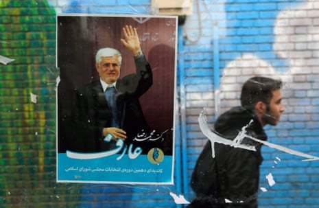 A man walks past a campaign poster of lead reformist candidate Mohmmad Reza Aref.