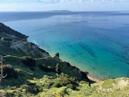 Land falling steeply towards a blue and green sea in sunny weather