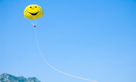 A girl parasailing under a yellow parachute with a smiley face