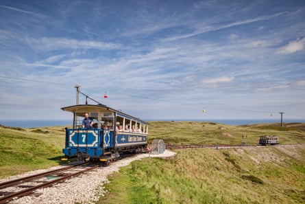 Vintage, open trams on a track up a grassy hill, with the sea in the distance