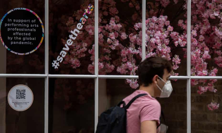 A man wearing a face mask walks past a shop in London with signs in the window supporting arts professionals, in July 2021