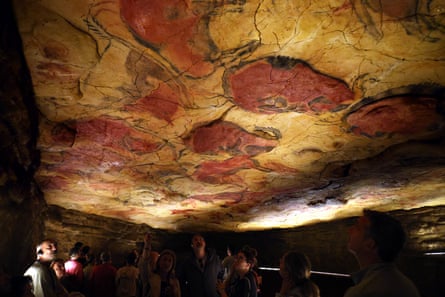 People looking up at ochre paintings of animals with charcoal outlines on a ceiling in a replica Cave of Altamira in Santillana del Mar, northern Spain