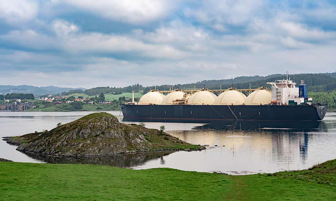 A large gas tanker on a body of water in Norway, surrounded by green grass and under a blue sky