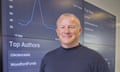 Neil Woodford smiling in front of a screen with analytics information on it