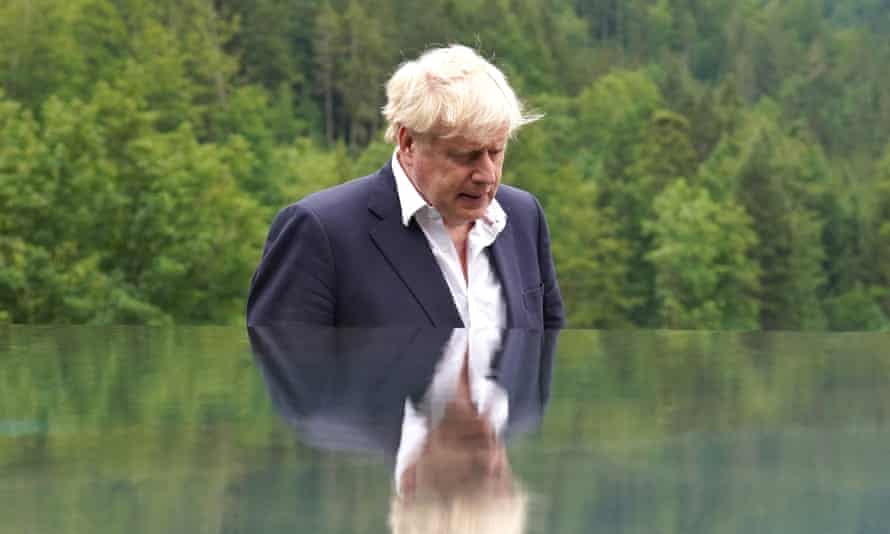 Boris Johnson outdoors, in a suit but no tie, with his head bowed.