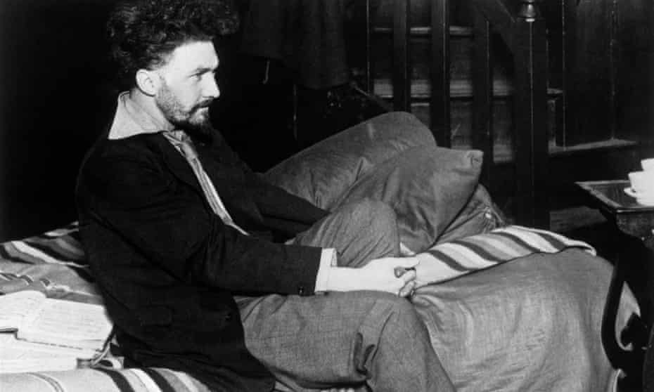 American poet and critic Ezra Pound sitting on his bed in his Paris studio in 1923.