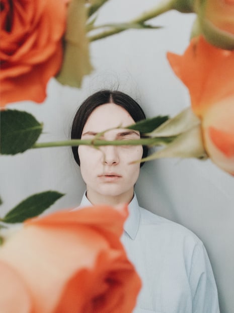 Photograph of a woman in a shirt, with her hair pulled back and the stem of a rose covering her eyes
