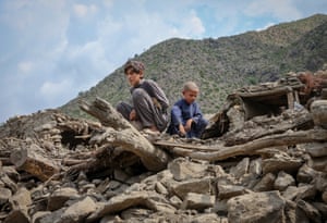 Two boys, looking sad, sit on a pile of rubble in the aftermath of the recent earthquake in a rural setting